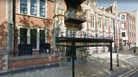 Pictured is East Staffordshire Borough Council building. It is a tall light red and white brick building with black railings.