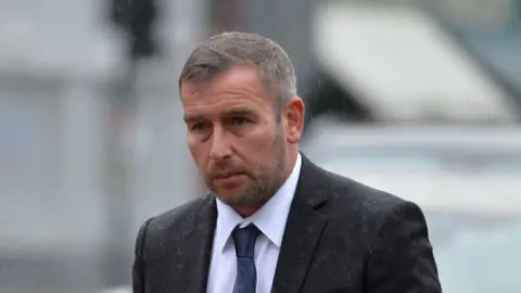 Scott Nugent - a man with short dark hair, wearing a suit, walking towards court