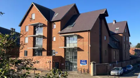 A large red brick building with a dark tiled roof and large glass windows