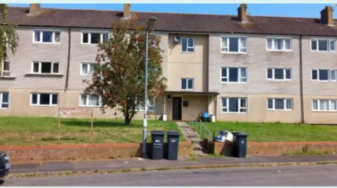 Somerset Council A three storey block of flats with a grass verge outside and bins on the pavement