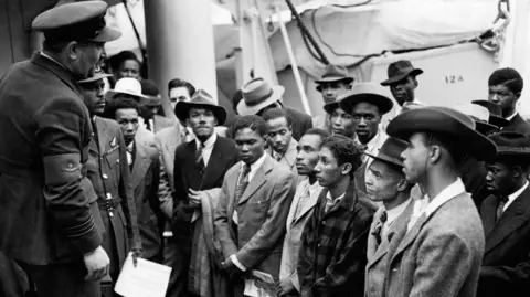 PA Media Black and white image of a row Jamaican immigrants welcomed by a RAF official from the Colonial Office after the ex-troopship HMT Empire Windrush landed them at Tilbury.