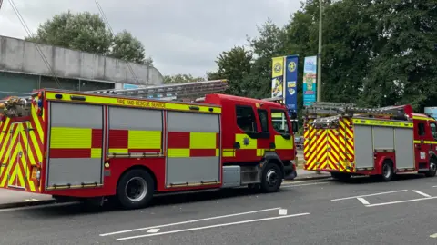 BBC Two fire engines parked on a road in front of a low-level, grey building