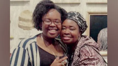Two women with arms around each other smile for the camera. 