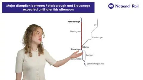 National Rail A map to the right on a white screen with a woman to the left who is pointing at it, like a weather forecaster. She has curly blonde hair and a cream coloured top. 