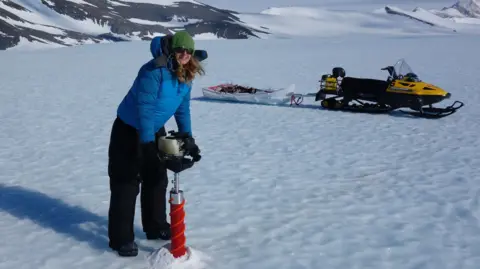 Dr Helen Millman A woman in cold weather gear stands on ice in the Antarctic, she is taking a core of ice to analyse as part of studies into the impact of climate change. Dr Helen Millman is a glaciologist and ice sheet modeller at the University of Exeter. 
