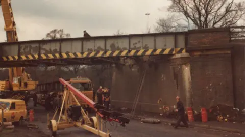 Supplied The colour photograph from 1975 shows the scene at the A5 bridge in Hinckley. Engineers are there and a crane and other vehicles and equipment can be seen. They are making a temporary repair. A year later a new bridge section was installed. 