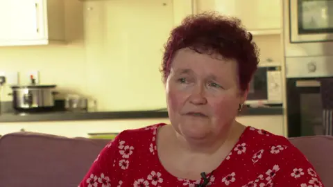 BBC Claire Throssell sits on a sofa wearing a red top dotted with white flowers.