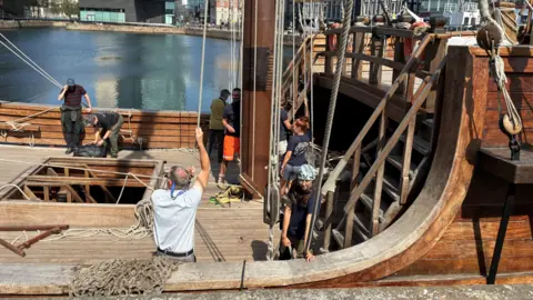 Tom Walker/BBC A large wooden ship crewed by a group of men and women