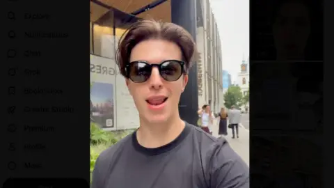 Cap/X A selfie style picture of Stephen Newnham who has short dark hair with a parting and is wearing sunglasses and a grey T-shirt.