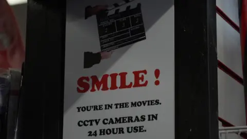 A sign in the fancy dress shop saying: "Smile! You're in the movies. CCTV cameras in 24 hour use".