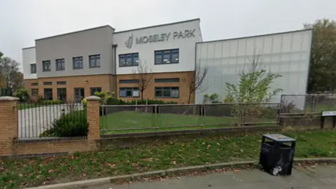 General view of Moseley Park Academy - a large white and beige rectangular building with the words Moseley Park in silver