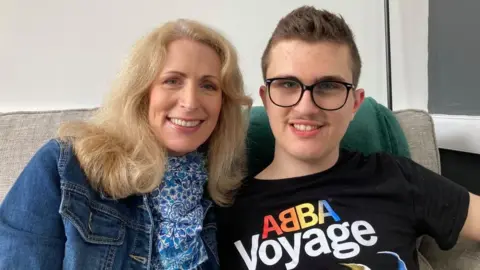 Alex Pope/BBC Suzanne and Zac Hollinshead sitting on a sofa and smiling to the camera