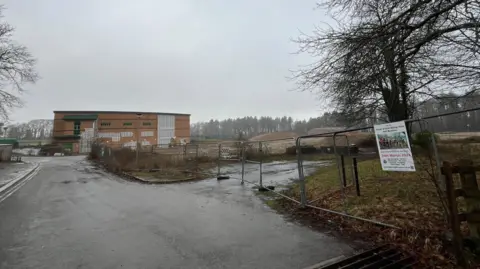 An abandoned college building in the Forest of Dean on a damp day. There is metal fencing around it.