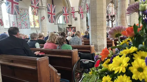 Richard Knights/BBC Interior of St Andrew's, Soham, showing people sitting in pews and Union Flags hanging in lines above