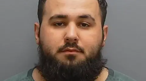 A custody shot of Rrahim Statovci, a man with short hair and a large beard. 