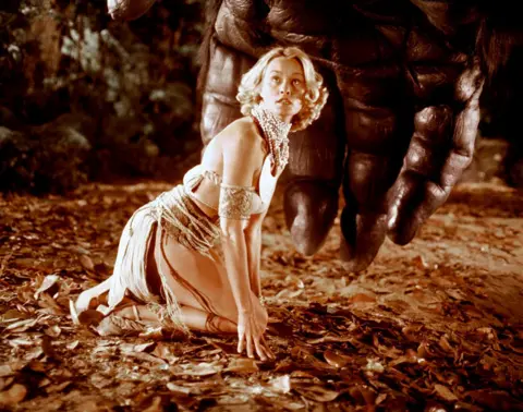 Getty Images Lange is in a skimpy dress, crouched on the ground while King Kong's very large and hairy hand looms over her. She looks alarmed.