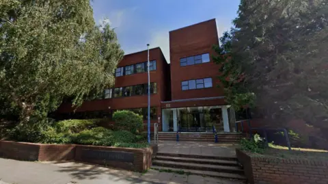 A brick building with stairs leading up to it. There are trees in the foreground.