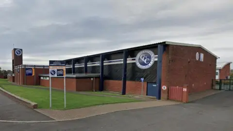 Churchill Community College. The school is made of red brick with blue supports.