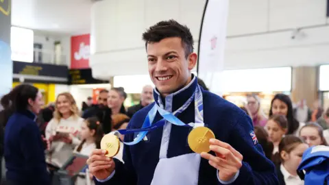 A man holding two gold medals and smiling.