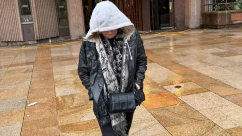 Helen Spree, 61,  who has blonde hair, walks away from Liverpool Magistrates' Court with her hood pulled up and wearing a black coat. 