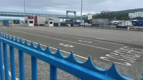The lanes for ferry traffic at the Sea Terminal - there are numbered lanes ticket booths at the end, and there is a blue spiked fence in the fore.