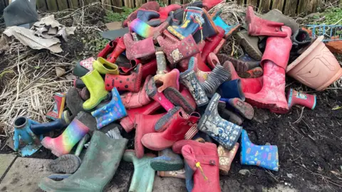 Simon Thake A huge pile of bright childrens' wellies sitting on a mound of earth