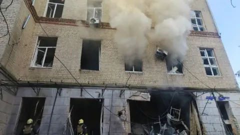 Smoke billows from a hospital in Sumy north-eastern Ukraine, as Ukrainian rescuers work on the site