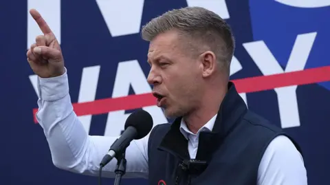 Sean Gallup/Getty Images A man in a gilet addresses an audience from a microphone