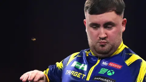 PA Media A wasp flies towards World Darts Champion Luke Littler at the oche during the final. He is wearing his signature purple and yellow darts top. 