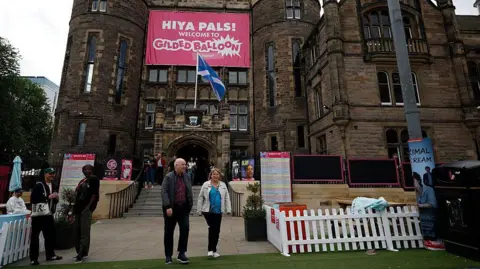 Getty Images People milling about the front of an Edinburgh Fringe venue with a pink banner saying 'Hiya Pals' on the front of it. 