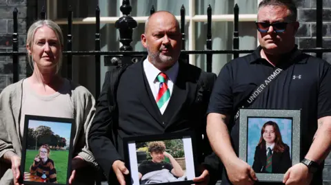 EPA Three parents standing outside Downing Street holding portraits of their children