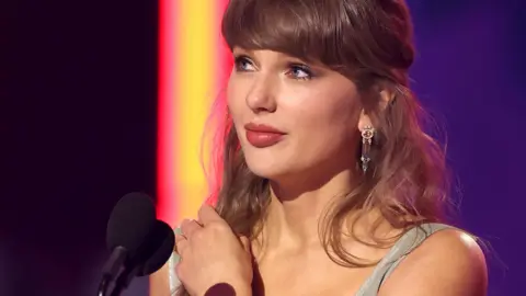 Taylor Swift looks away from camera while speaking into a microphone onstage at the iHeartRadio music awards in LA in March.