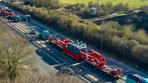 Aerial photo of a large convoy of vehicles passing on a main road through green countryside