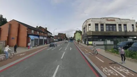 Sheffield City Council Artist impression of the main route through Attercliffe complete with red route lines, separate red cycle lanes on both sides of the carriageway, and a main road mainly free of traffic, except for two cars and a blue bus in the distance. The illustration features three cyclists, shop fronts (many of which are closed) and the former Burton building. 