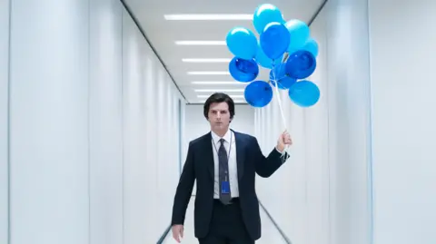 Apple TV Adam Scott as Severance's Mark Scout holding blue balloons in a sanitised white office hall