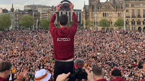Captain Richie Smallwood with promotion shield in front of fans