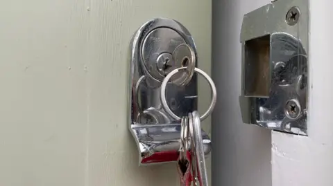 The image shows keys in a lock in a door. The door is ajar.