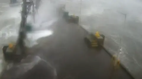 Storm Éowyn waves crashing across a pier with grey waves and spray.