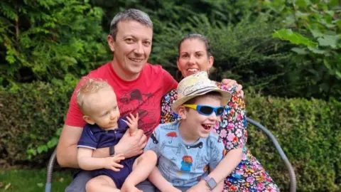 Family Handout A man sits with his arm around a woman and two young children sit on their laps
