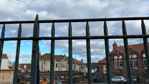 A picture of Fairlawn primary school in Montpelier in Bristol behind the iron fence with clouds above and a row of houses behind it. 