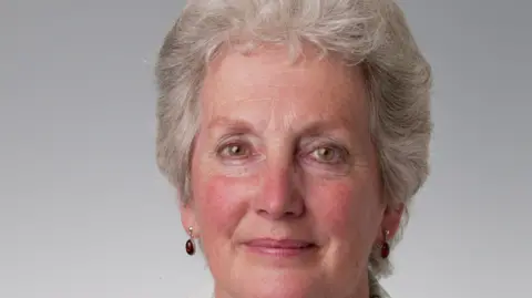 BBC/Flying Colours A picture of a smiling woman with short white hair. She is wearing gem earrings