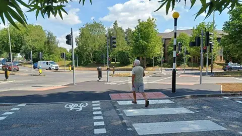 A man in shorts strutting across the road on the new zebra crossing