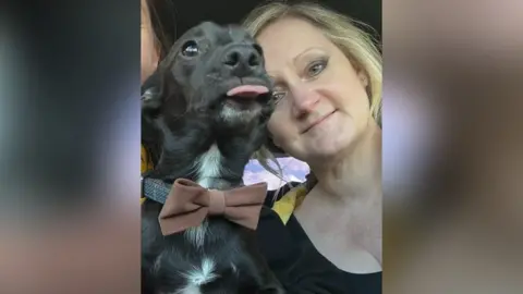 Melanie Gassman Melanie Gassman, who has blonde hair, next to her dog Harry, who has black wiry fur and is wearing a dark red bow tie