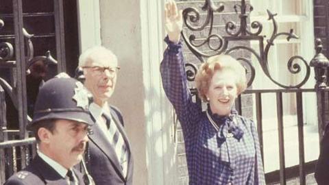 Margaret Thatcher waving standing outside 10 Downing Street, accompanied by husband Dennis.  A policeman is seen in the foreground.
