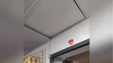 Oxfordshire County Council A picture from inside the raided shop showing a ceiling concealment. There is a security sticker on the wall under it. Yellow bottles of a sweet drink are lined on a nearby shelf.