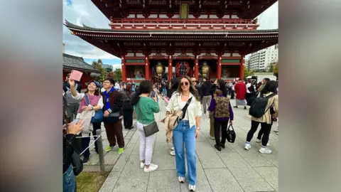 Shannon Griffiths Woman, Shannon, poses for tourist photo in front of a what appears to be a temple in Asia.