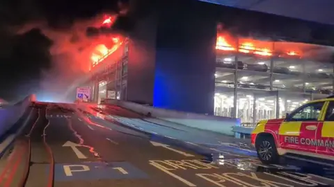 PA Media A fire command vehicle is parked near the burning car park building