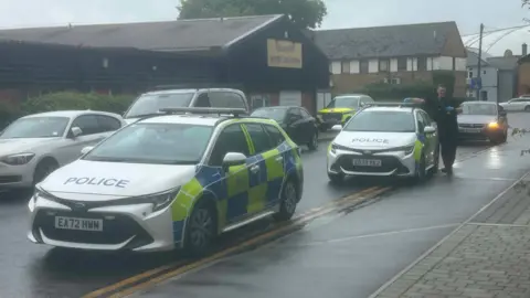 Two parked police cars and an officer by the pavement in a residential street.