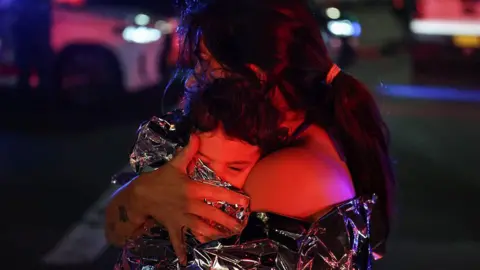 Getty A woman hugs a child wrapped in a foil blanket to her