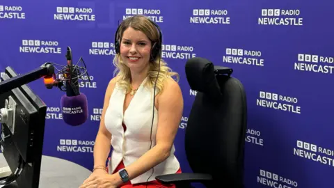 Kim McGuinness sitting in front of a microphone in the BBC Radio Newcastle studio